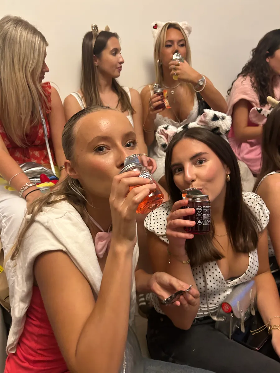 Two friends in fancy dress each taking a sip from a FizzBomb can