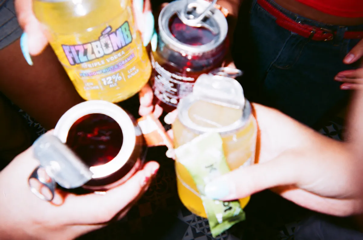 Close-up of friends clinking FizzBomb cans, Party Powder sachets in hand