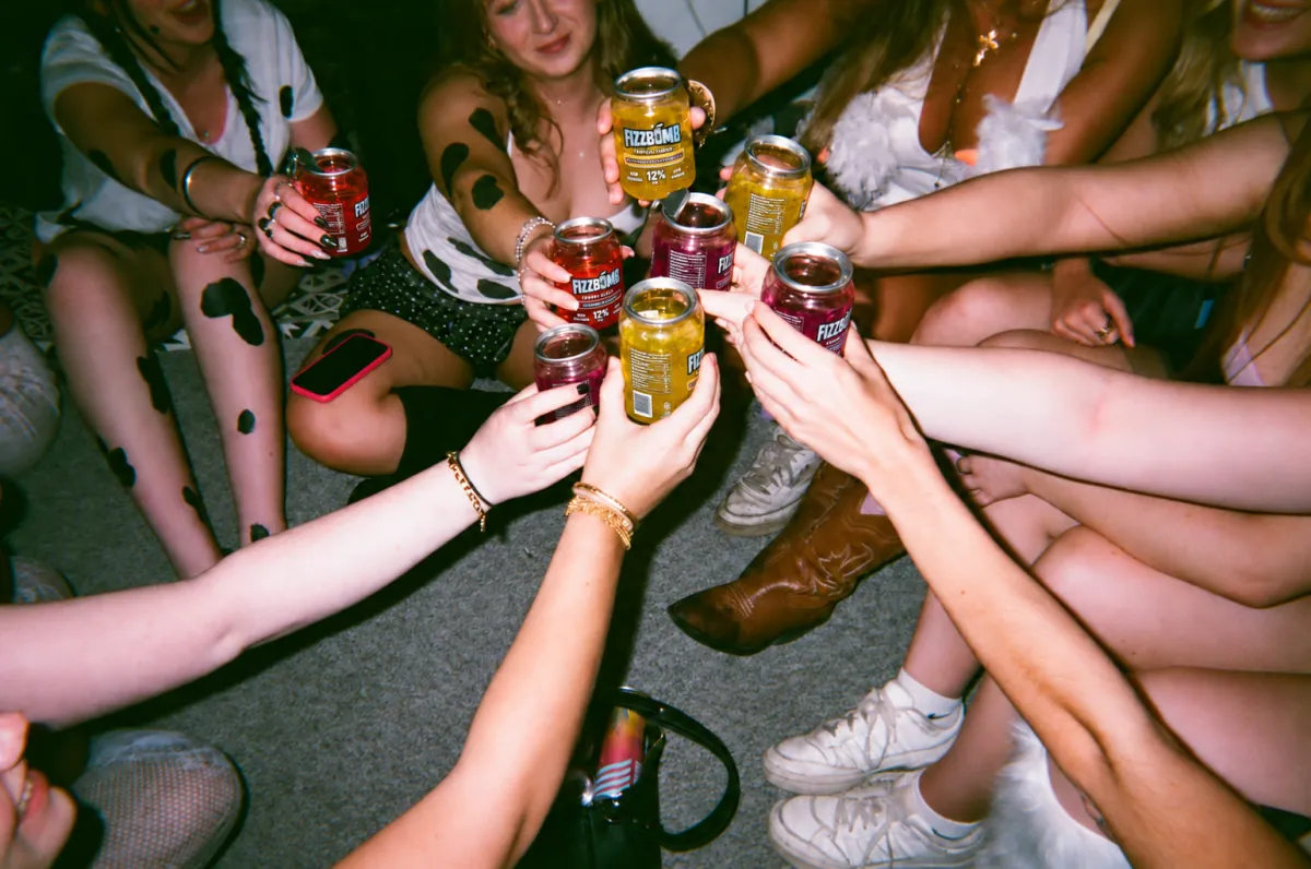 A circle of friends on the floor clinking their FizzBomb cans