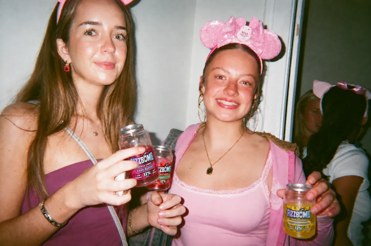 Two friends in party ears smiling with their FizzBomb cans