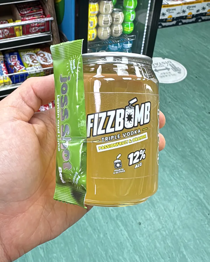A FizzBomb Passion Fruit & Orange can held up in a corner shop