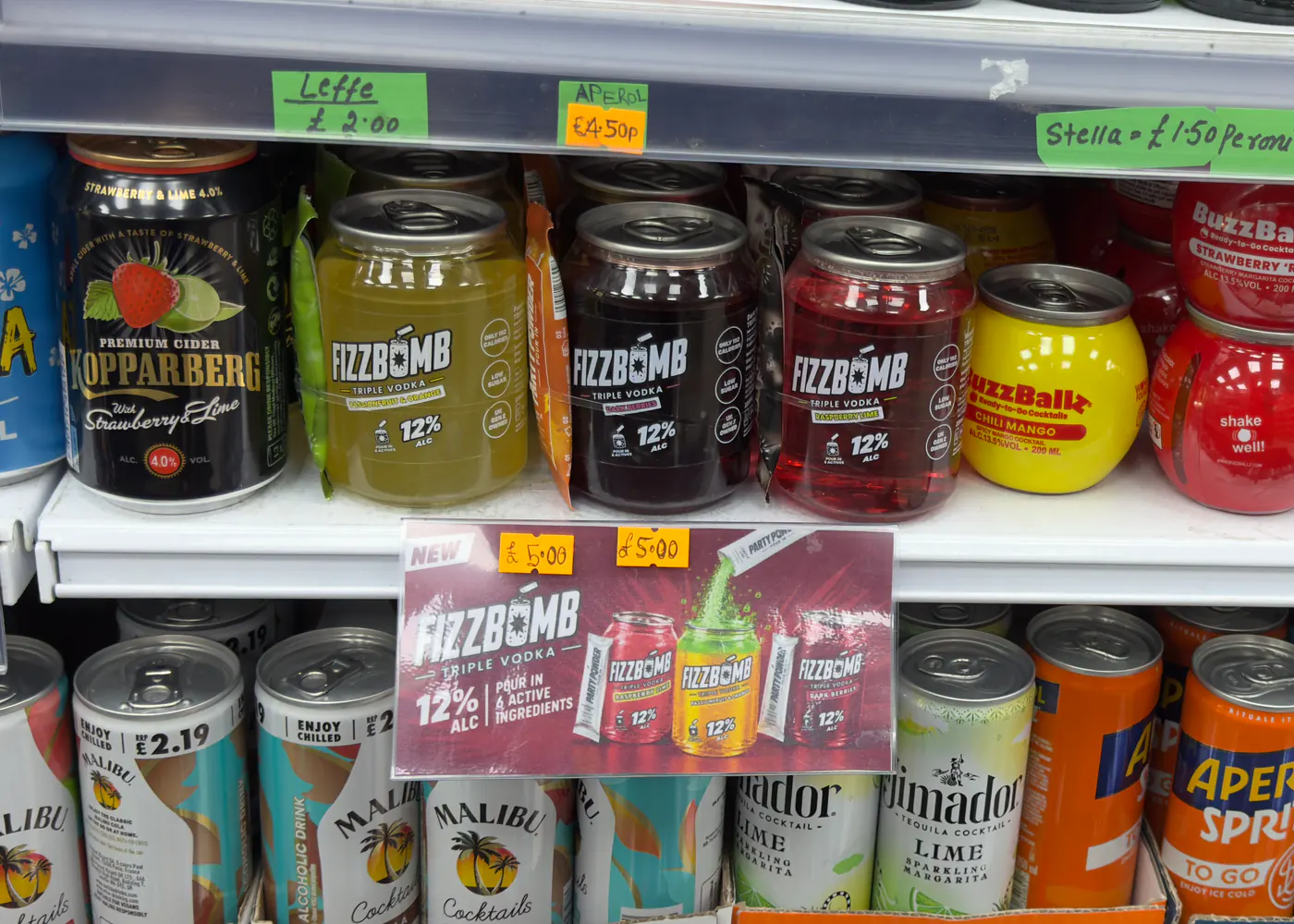 Passion Fruit & Orange, Dark Berries and Raspberry Lime FizzBomb cans in a shop fridge between Kopparberg and BuzzBallz, above a New FizzBomb shelf card priced £5.00