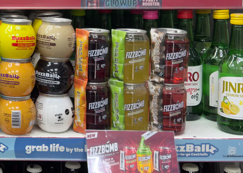 Two rows of FizzBomb cans on a shop shelf between BuzzBallz and Jinro soju, with a New FizzBomb card on the shelf edge